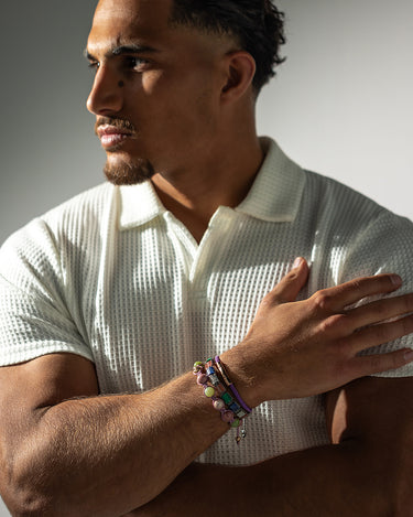 Man in witte polo met handgemaakte armband in paars en goudkleurig. Luxe heren sieraden voor een elegante uitstraling.